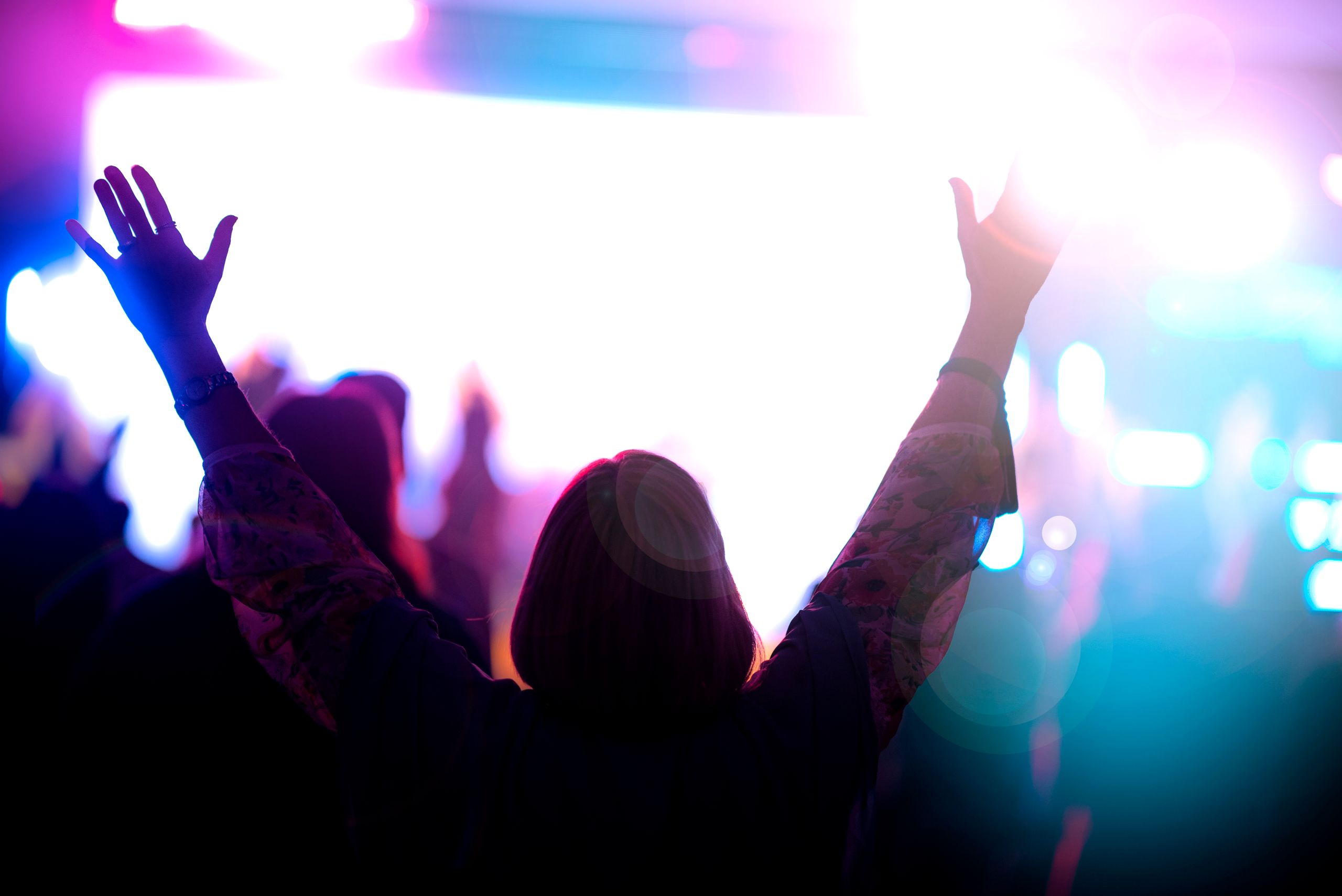 A dynamic silhouette of an audience member with arms raised at a vibrant nighttime concert.