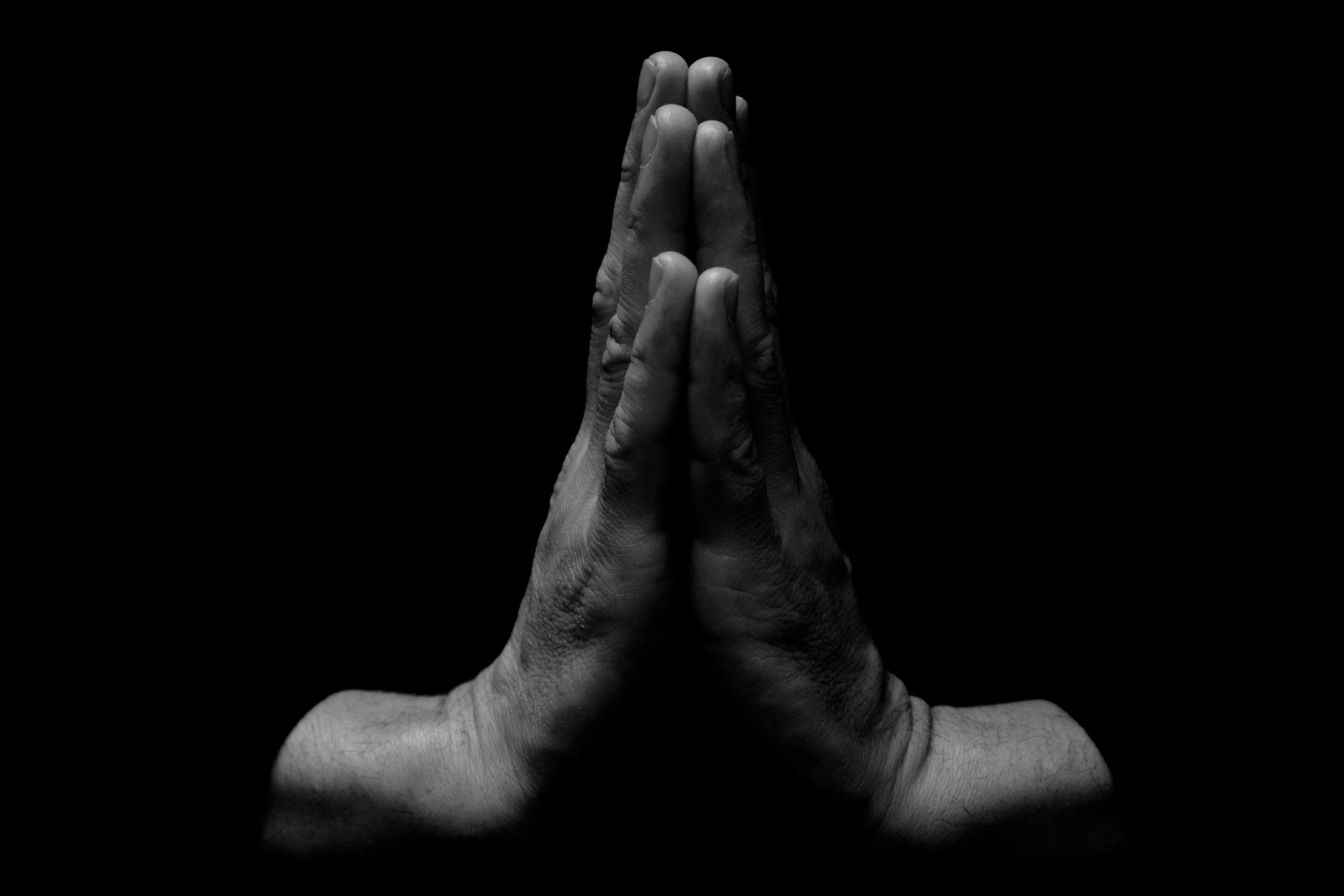 Close-up of clasped hands in a praying position on a black background, emphasizing unity and spirituality.